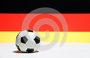 Small football on the white floor with black red and yellow color of German nation flag background.