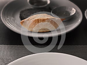 Small French bread baguette on white plate, wooden table copy space, selective focus, monotone background