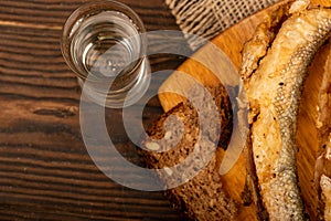 A small fried fish on a wooden board, pieces of bread and a glass of vodka, close-up, selective focus