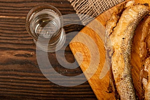 A small fried fish on a wooden board, pieces of bread and a glass of vodka, close-up, selective focus