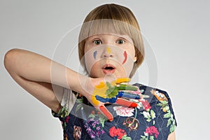 A small frightened girl covers her face with a paint-stained hand