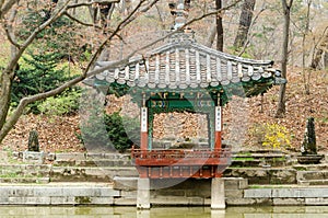 A small gazebo sits in a park with a pond in the background