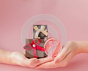 Small gift boxes in women`s hands on a pink background. Festive concept for Valentine`s day, Mother`s day or birthday