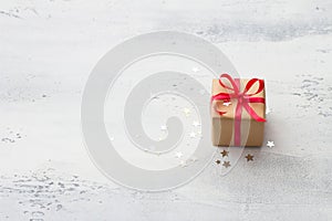 A small gift wrapped in kraft paper with a red ribbon on a light blue background with natural Christmas tree branches