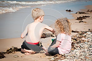 Small giirl watches her brother exploring and playing in the sea