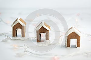 Small gingerbread houses for a cup on white background next to garland. Christmas baked goods