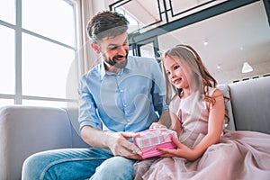 Small girl adn her dad holding gift box sitting on the couch at home