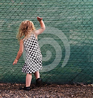 Small girl banging on a green fence