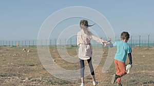 Small girl and boy refugees walk in desert towards fencing with barbed wire. Kid holds plush toy in his hand concept of forced imm