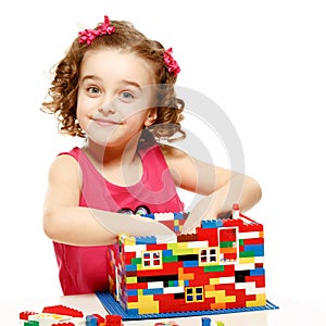 Small girl builds a house from plastic blocks