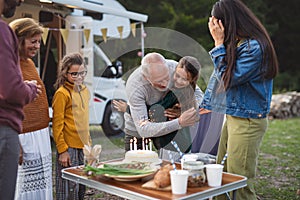 Small girl celebrating birthday outdoors at campsite, multi-generation family caravan holiday trip.
