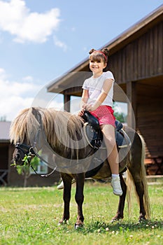 Small girl with cute hairstyle sitting on the horse and smiling