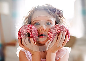 A small girl with doughnuts at home, looking at camera.