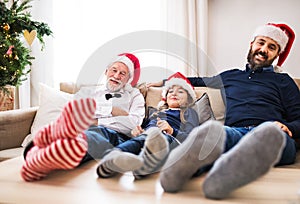 A small girl with father and grandfather sitting on a sofa at Christmas time.