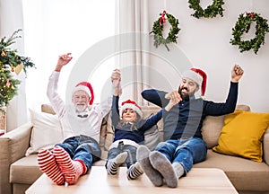 A small girl with father and grandfather sitting on a sofa at Christmas time.