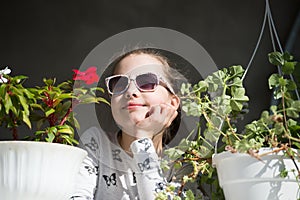 Small girl with flowers. Fashion child wear sunglasses on sunny day. Beauty kid with plant pots in summer or spring. Freshness and