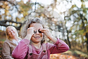 Small girl with grandmother on a walk in autumn forest, having fun.