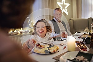 Small girl with grandparents sitting indoors celebrating Christmas together.