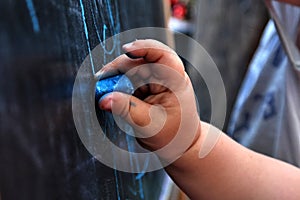 Small girl hand drawing picture on blackboard with blue chalk