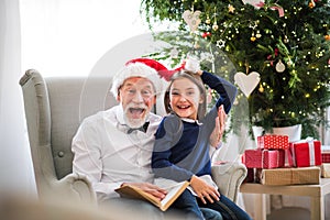 A small girl and her grandfather with Santa hat and a book at Christmas time.