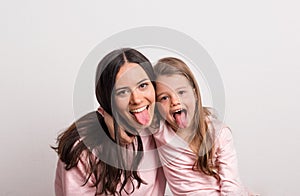 A small girl and her mother sticking tongues out in a studio.