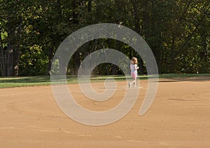 Small girl kicking up dust on a smoothly raked baseball infield