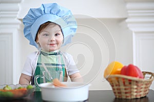 Small girl in kitchen apron and cap play at table photo