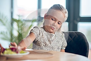 A small girl looking unpleased while looking at the food on the table