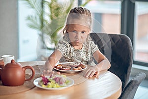 A small girl looking unpleased while looking at the food on the table