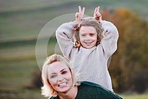 Small girl with mother on a walk in autumn nature, having fun.
