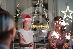 Small girl with parents and grandparents with sparklers indoors celebrating Christmas.