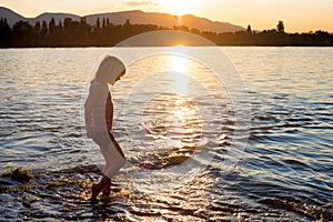 Small girl playing in river water at sunset