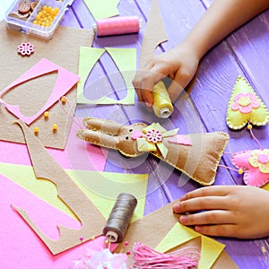 Small girl shows a felt bunny in hands. Girl made a felt cute bunny with hearts for Easter. Tools and materials for kids