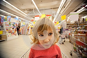 Small girl sit in shoppingcart in supermarket