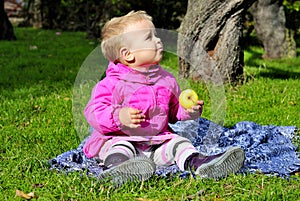 Small girl sits on green glade with apple