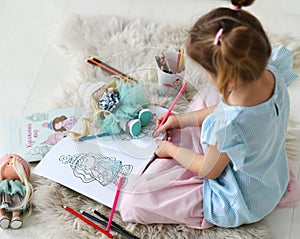 Small girl sitting on soft carpet and coloring doll drawing with colorful pencils at home, top view. Happy childhood