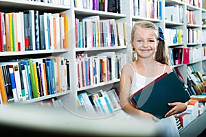 Small  girl standing in book store and taking  literature