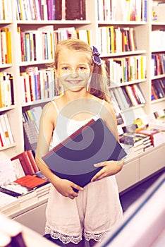 Small girl standing in book store and taking literature