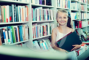 Small girl standing in book store and taking literature