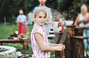 A small girl standing outdoors on a barbecue grill party in the backyard.