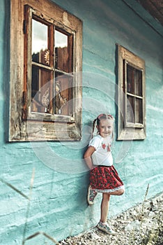 Small girl in traditional skirt posing in traditional village with wooden cottages