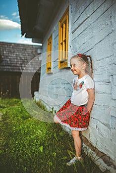 Small girl in traditional skirt posing in traditional village with wooden cottages