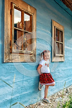 Malé dievča v tradičnej sukni pózuje v tradičnej dedine s drevenými domčekmi