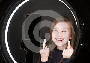 Small girl using camera of smartphone in front of ring light, shooting video for blog. Adorable child learning new technology.