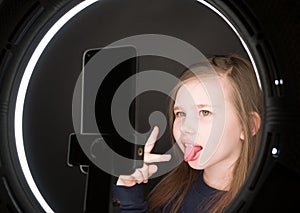 Small girl using camera of smartphone in front of ring light, shooting video for blog. Adorable child learning new technology.