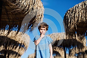A small girl walking among straw parasols outdoors on beach.