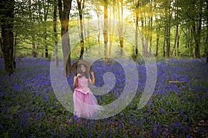 Small girl walks through bluebell woods in pink dress