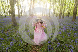 Small girl walks through bluebell woods in pink dress