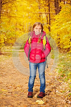 Small girl wears rucksack and stands in forest