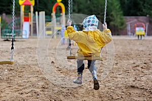 Small girl in yellow rain coat on swing